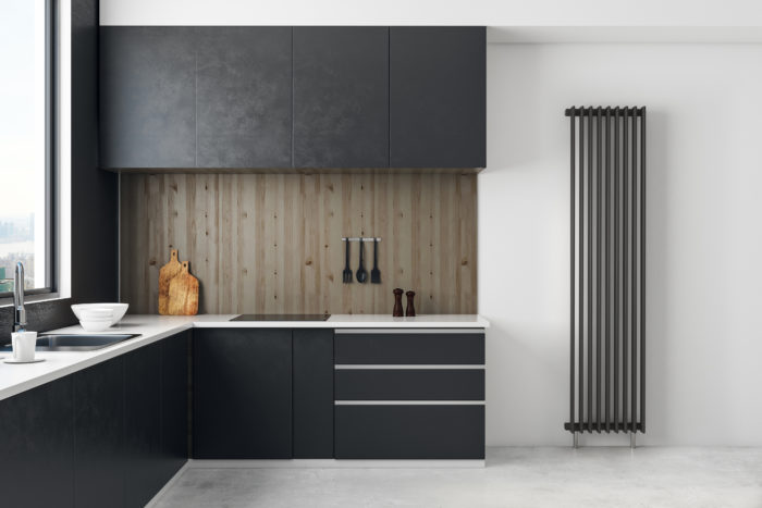 QRL Radiator Photomontage, Product Visualisations, Deep Grey minimal, built in kitchen on the left, with vertical wood panelling back splash, white floor and walls, vertical radiator render on the right, from floor to just below full ceiling height. Produced by the team at G-Net3D